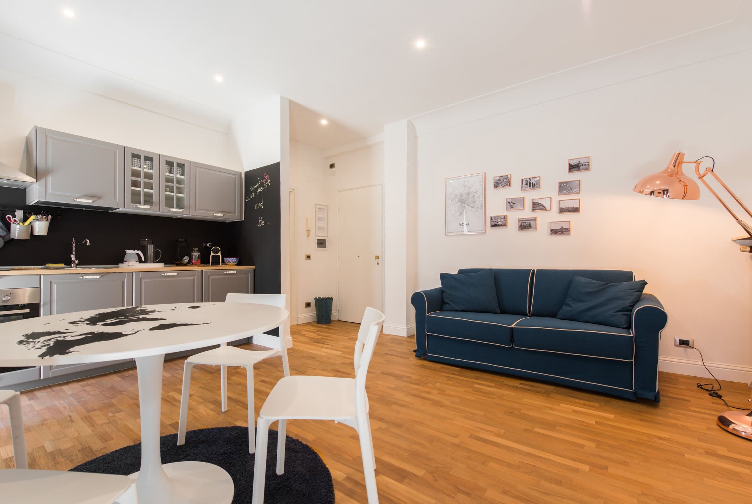 The open-plan living room with the kitchen, blue sofa and copper lamp